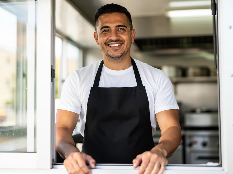 Marco Reyes, founder of Flat Iron, standing at the truck service window in black apron